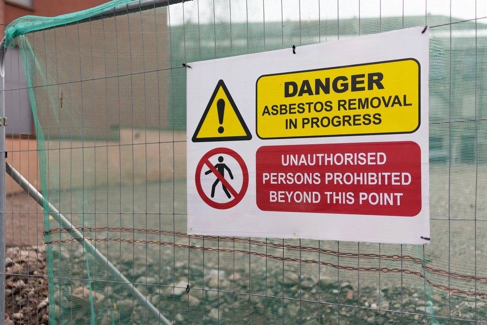 Construction site warning sign reading “Danger: Asbestos Removal in Progress – Unauthorized Persons Prohibited Beyond This Point