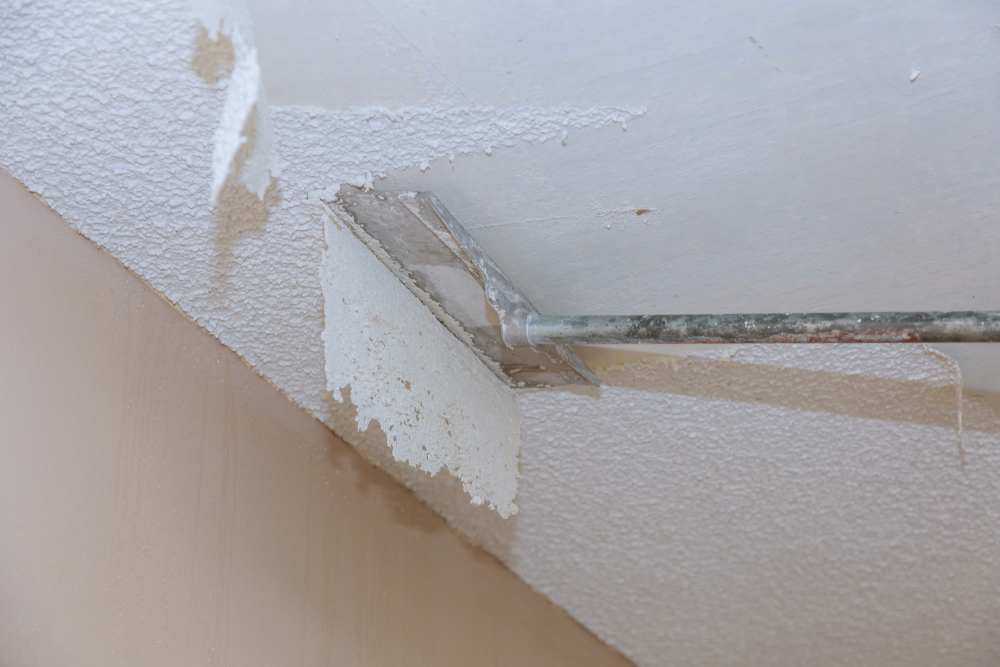 Worker removing asbestos-containing popcorn ceiling texture with a scraper