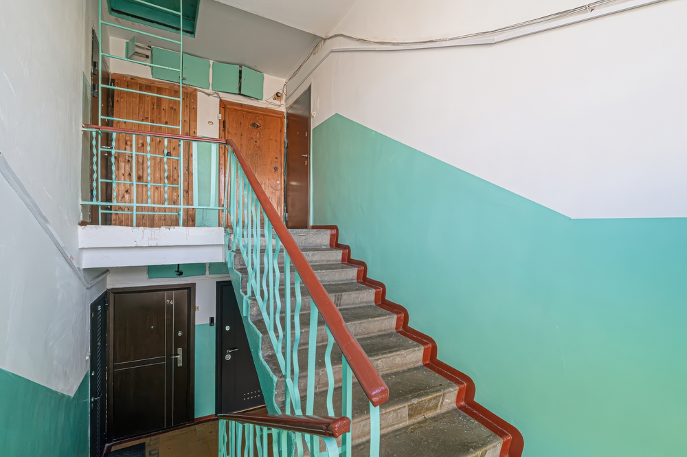 Interior stairwell of an older building with painted turquoise walls, metal railings, and worn concrete steps