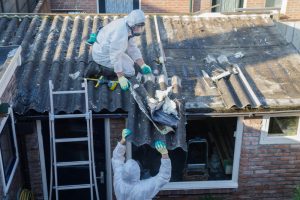 Professional team in protective suits removing asbestos cement from corrugated roofing
