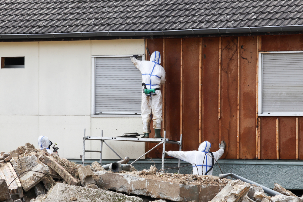 Professionals in protective suits remove asbestos on a wall