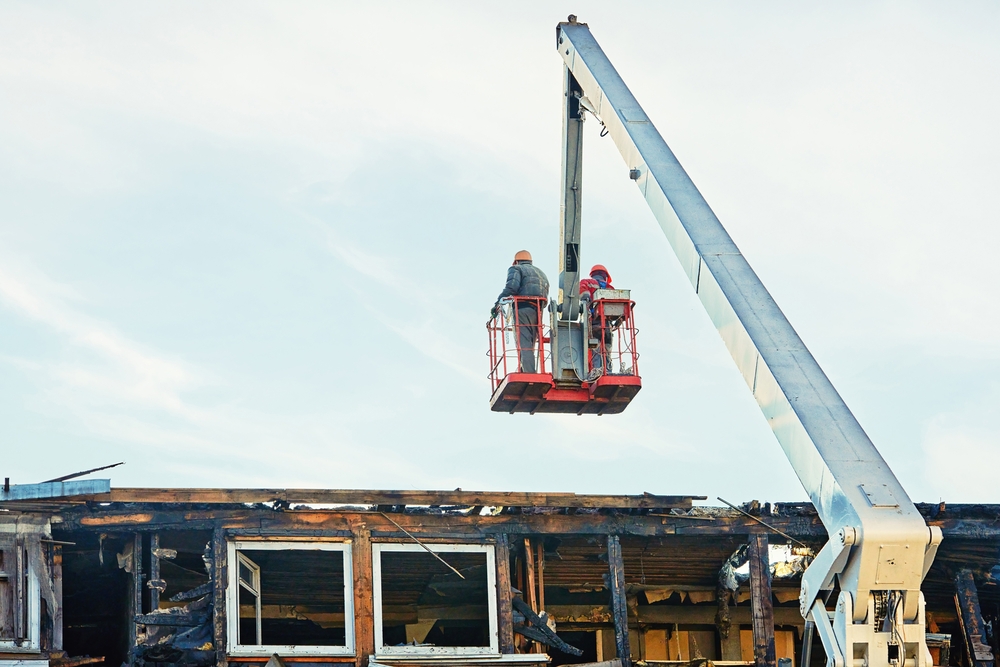 Workers on crane cradle dismantle burnt roof after a fire