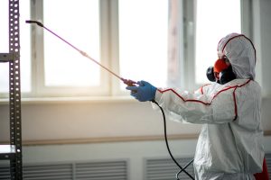 Environmental remediation specialist in a protective suit and respirator applying mold treatment inside a commercial facility