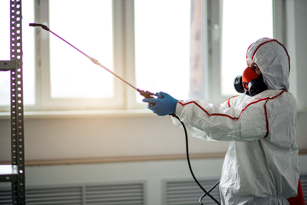 Environmental remediation specialist in a protective suit and respirator applying mold treatment inside a commercial facility